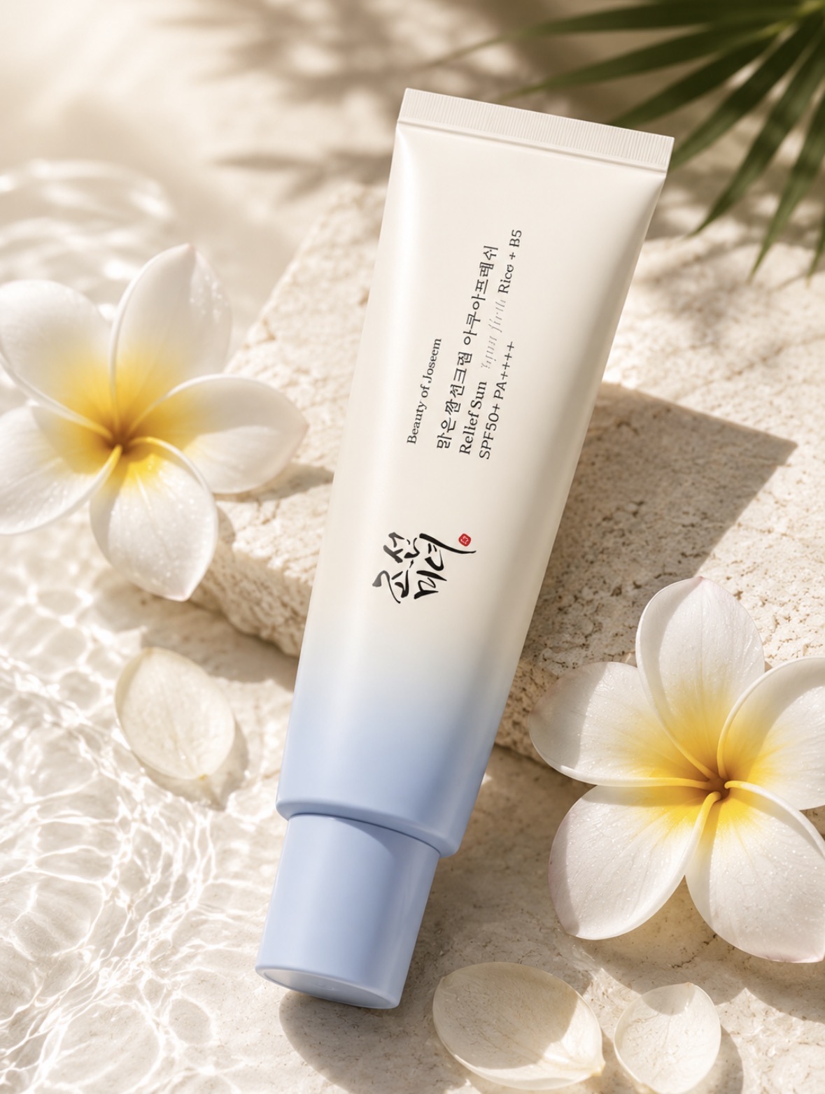 Crème solaire Beauty of Joseon Relief Sun posée sur une pierre ivoire, eau claire et plumerias blancs