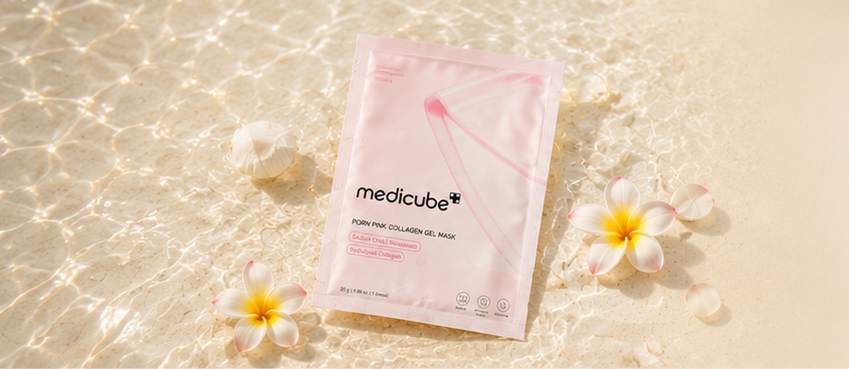 Masque en gel de collagène Medicube posé sur le sable ivoire au bord d'une eau claire, fleurs de plumeria blanches